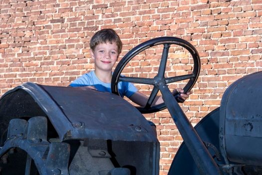 a boy driving an old vintage tractor in the background of a brick wall.