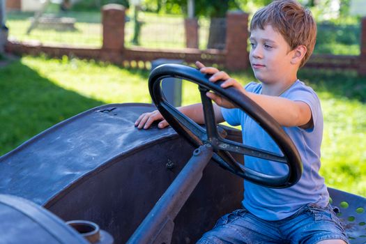 a boy driving an old vintage tractor. Happy Caucasian preschool boy having fun in the summer on an old tractor outdoors, pretending to drive an old tractor
