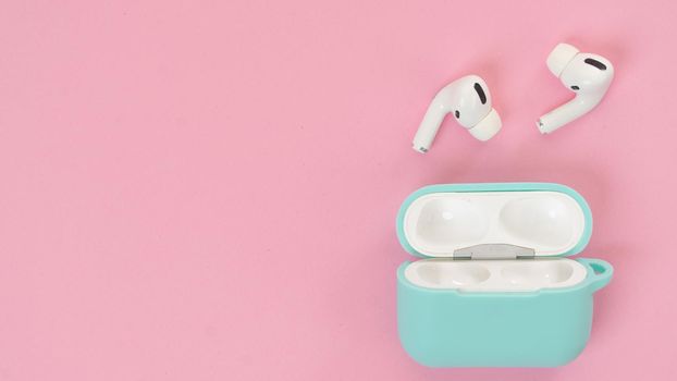 Wireless headphones in mint case on pink background, delicate background shades with space for text. High quality photo
