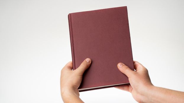 Men's hands hold a book or notebook in a burgundy binding on a white background. High quality photo