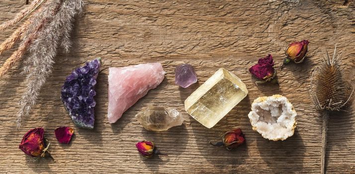 Amethyst druzy, pink quartz, quartz with rutile, fluorite, calcite, quartz in geode mineral stones set up on the wooden table with dry flowers. Gemstones for esoteric spiritual practice or witchcraft 