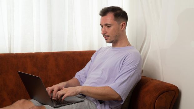 A man works at a laptop on the couch, remote work, homeschooling. High quality photo