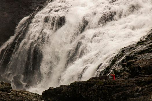 Woman in red dress dancing above Kjosfossen waterfall close to Flam tourist town in Norway