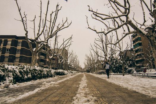 Winter pedestrian snowy long street and a man walking in Igualada town in Barcelona province