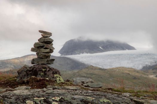 Landscape showing a foggy mountain behind a snowy valley and stone landmarks in the foreground in Norway