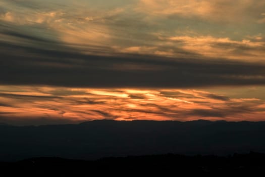 Landscape showing a cloudy and orange sunset over the mountain