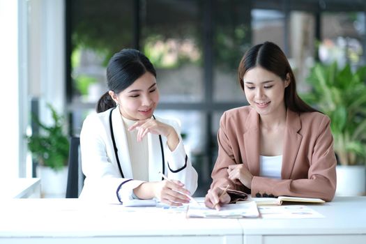 Two young Asian businesswoman discuss investment project working and planning strategy. Business people talking together with laptop computer at office..