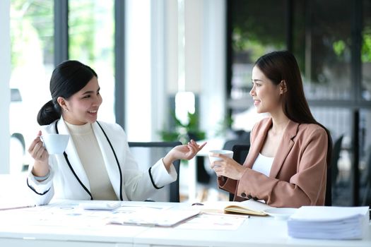 Young Asian woman talk work together successfully hold coffee cups and cheers at office