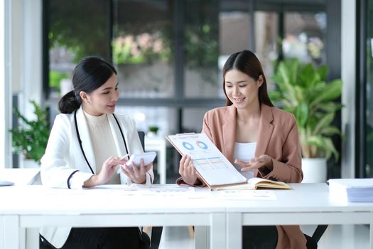 Two young Asian businesswoman discuss investment project working and planning strategy. Business people talking together with laptop computer at office..