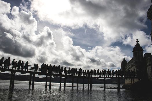 Queue of people silhouettes entering to tourist Belem tower under a cloudy sky in Lisbon in Portugal