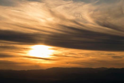 Landscape showing a cloudy and orange sunset over the mountain