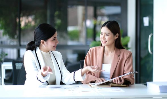 Two young Asian businesswoman discuss investment project working and planning strategy. Business people talking together with laptop computer at office..