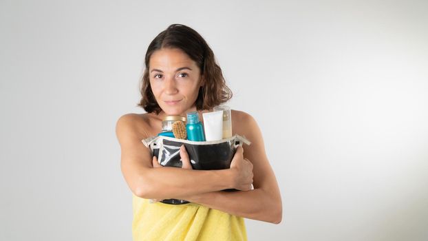 A woman in a towel hugs a cosmetic bag with creams, serum and cosmetics for body and face care. High quality photo