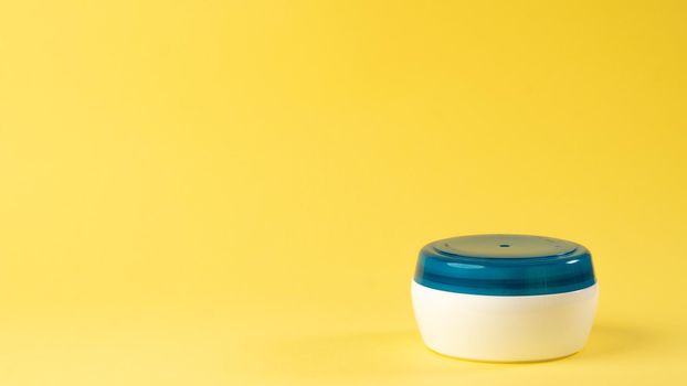 White jar of cream with green lid on a yellow background, home care. High quality photo