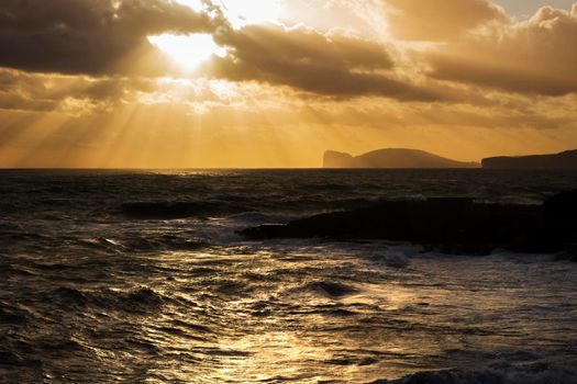 Seascape in the evening showing waves and rocks under a cloudy sky from Alghero in Sardegna island in Italy