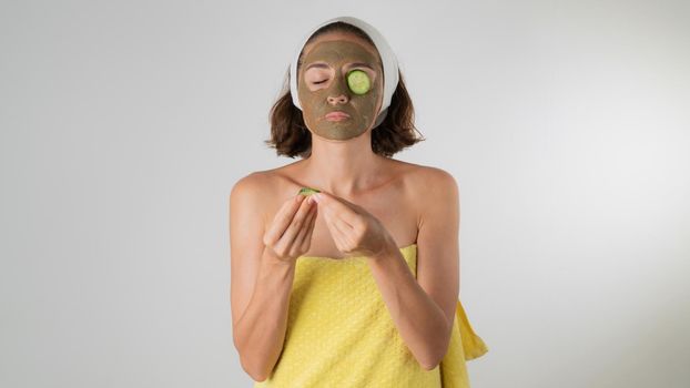 A woman in a clay mask puts a circle of cucumber on the eye - facial skin care at home. High quality photo