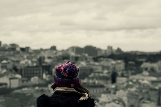 A girl wearing a wool cap looking at Barcelona cityscape from above