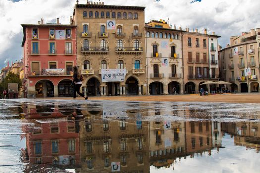 Classic building facades in a square and its reflection on a big puddle in Vic town in Catalonia