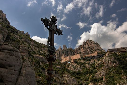 Mountainous landscape showing tourist Montserrat Monastery and a cross with Jesus Christ in the foreground in Montserrat Barcelona