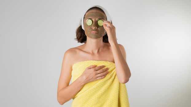 Woman in a towel with a mask on her face and circles of cucumber on her eyes - home care. High quality photo
