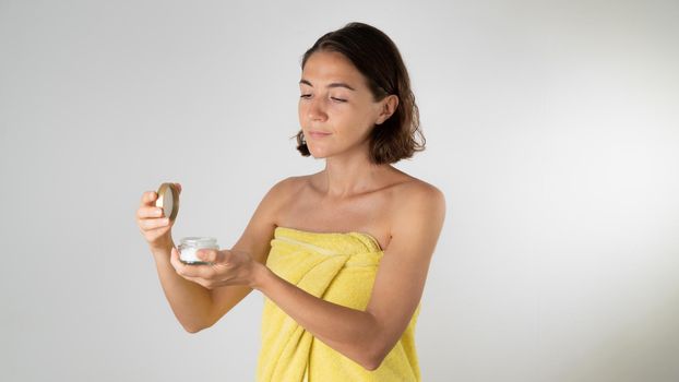 A woman after a shower holds a jar of cream in her hands - skin care of the body and face. High quality photo