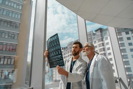 Two doctors in uniform look and discuss an X Ray or MRI scan of the patient spine in clinic