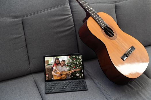 Acoustic guitar and digital tablet on a couch at cozy home background. Online music lessons, learning playing or writing songs and hobby concept.