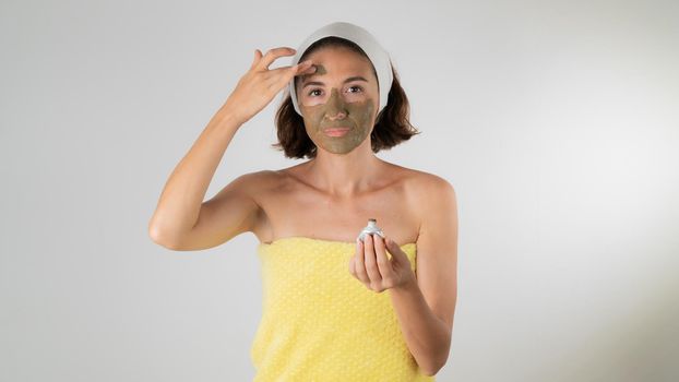 A woman in a towel after a shower applies a clay mask to her face - self-care at home. High quality photo