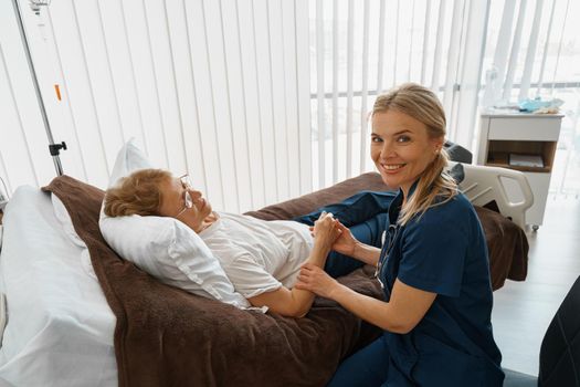 Doctor therapist holding hand of patient in hospital ward and looking camera. High quality photo