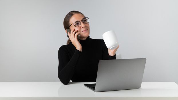 An office worker with a laptop talks on the phone and holds a cup of coffee in her hand. High quality photo