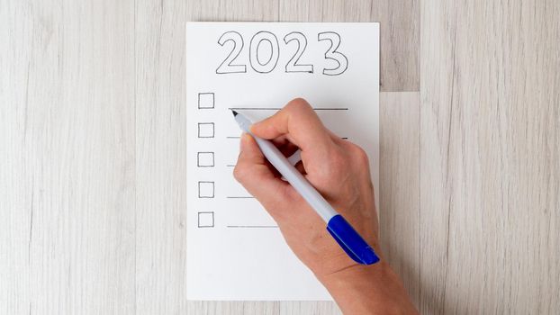 A woman's hand fills the checklist with a pen for the new year 2023. High quality photo