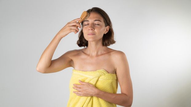 A woman in a towel brushes along the massage lines of the face - self-care at home. High quality photo