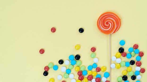 Sweets on a bright colored background - lollipop and multi-colored dragee with space for text. High quality photo