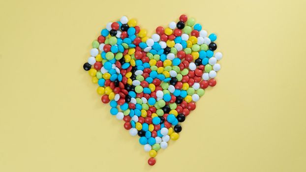 Heart of sweet multi-colored dragees on a yellow background. High quality photo