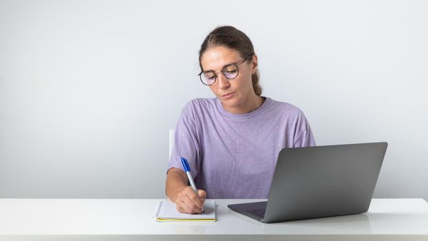 The girl sits at the laptop and makes notes in the notebook, study, work. High quality photo