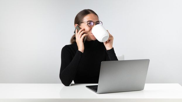 Woman at laptop talking on the phone and drinking coffee - workplace. High quality photo