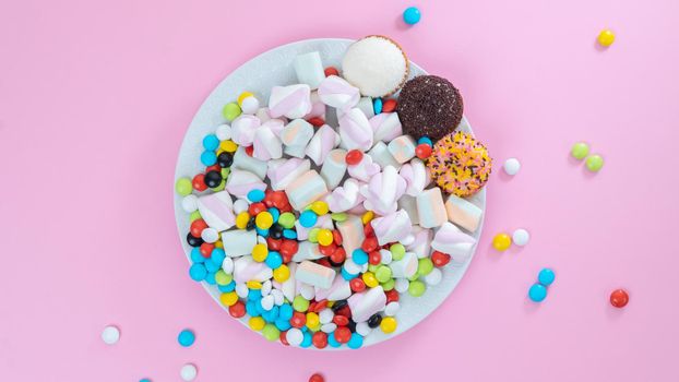 Colorful sweets on a plate on a pink background - sugar food. High quality photo