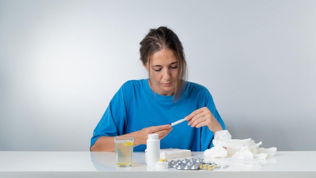 A woman with the flu checks the temperature - treatment at home with pills. High quality photo