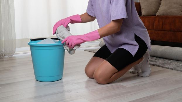 A woman in rubber gloves squeezes a rag in a bucket washes the floor. High quality photo