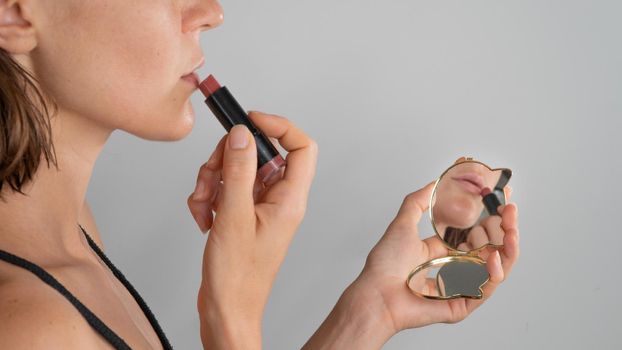 The girl paints her lips with lipstick in a pocket mirror, reflection - makeup. High quality photo