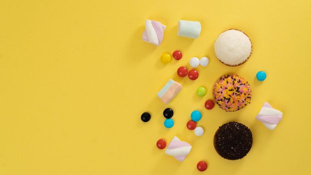 Cakes, marshmallows, sweets on a yellow background - sweets and space for text. High quality photo