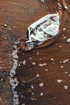 plastic bag on the beach, seashore and water pollution with plastics concept, trash at the seaside, top view of an environmental problem with wave of water and sand