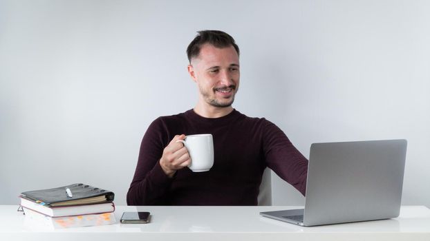 An employee negotiates a video connection in a laptop with a mug of coffee, work in the office or freelance at home. High quality photo