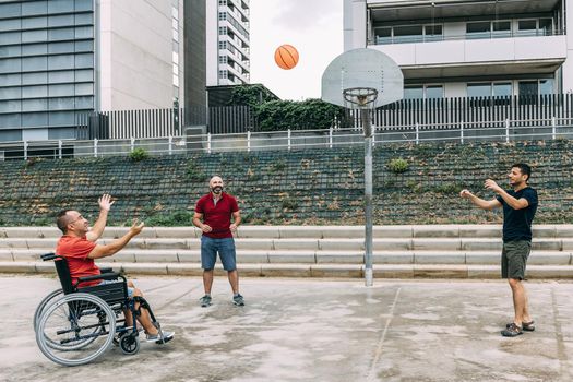 joyful disabled man in wheelchair playing basketball with friends with a ball, concept of adaptive sports and physical activity, rehabilitation for people with physical disabilities