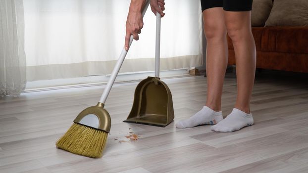 The housewife does the cleaning in the apartment sweeps the dirt off the floor with a broom brush into the scoop. High quality photo