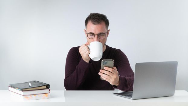 A man at work drinks coffee and looks at a smartphone. High quality photo