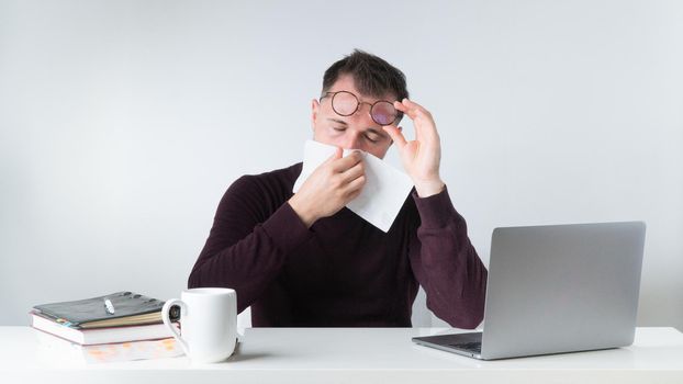 A man wipes his nose with a napkin - runny nose, flu, cold at work, get sick in the office. High quality photo