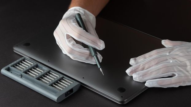 The master repairs a laptop in white gloves with a screwdriver and a set of bits. High quality photo