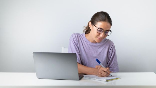 A student at a laptop makes notes in a notebook, studies. High quality photo