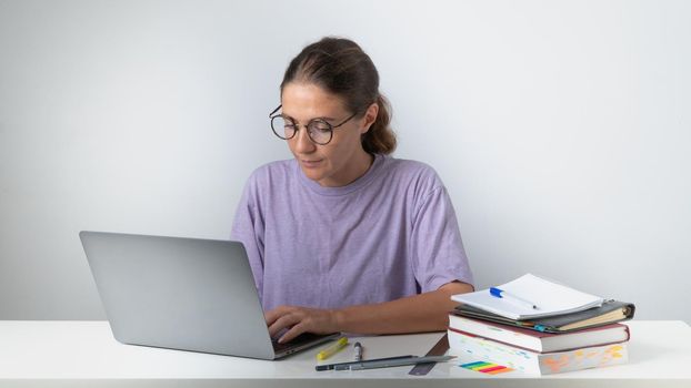 A woman prints on a laptop at a table with books and notebooks. High quality photo